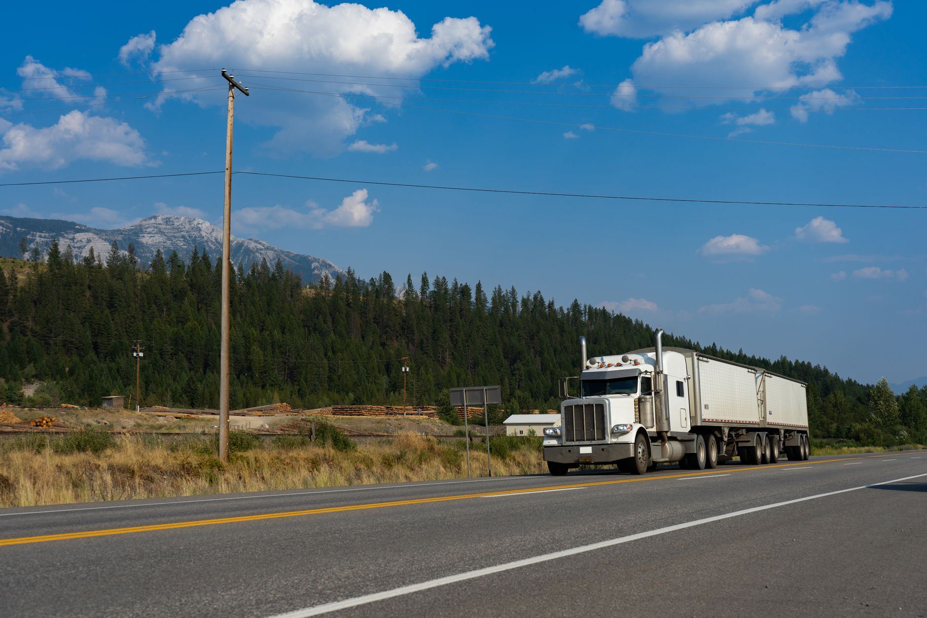 A white semi-truck traveling on a scenic road in Jaffray, BC, with mountains in the backgr