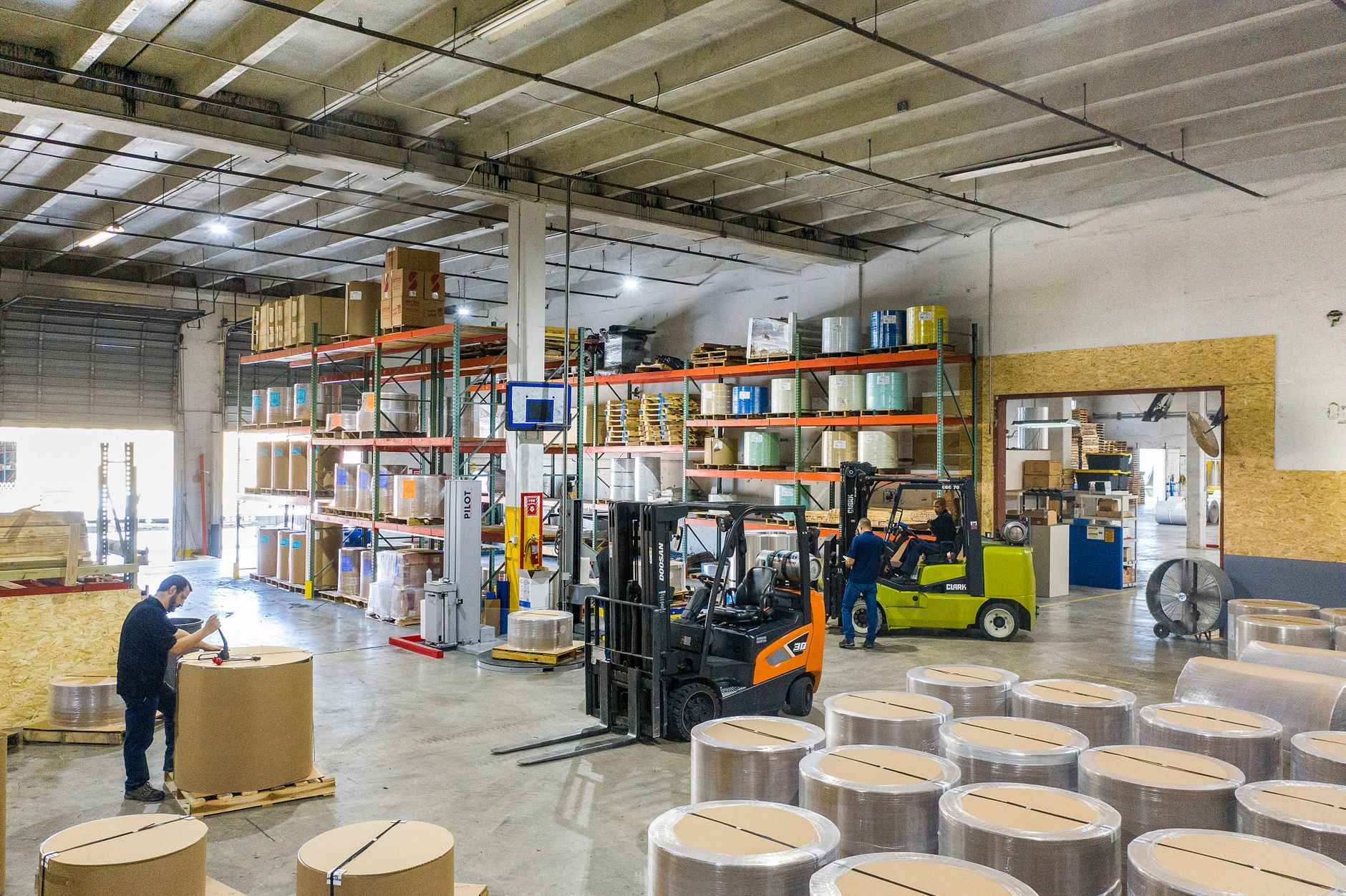 Interior view of a busy warehouse with forklifts and workers handling large rolls of mater